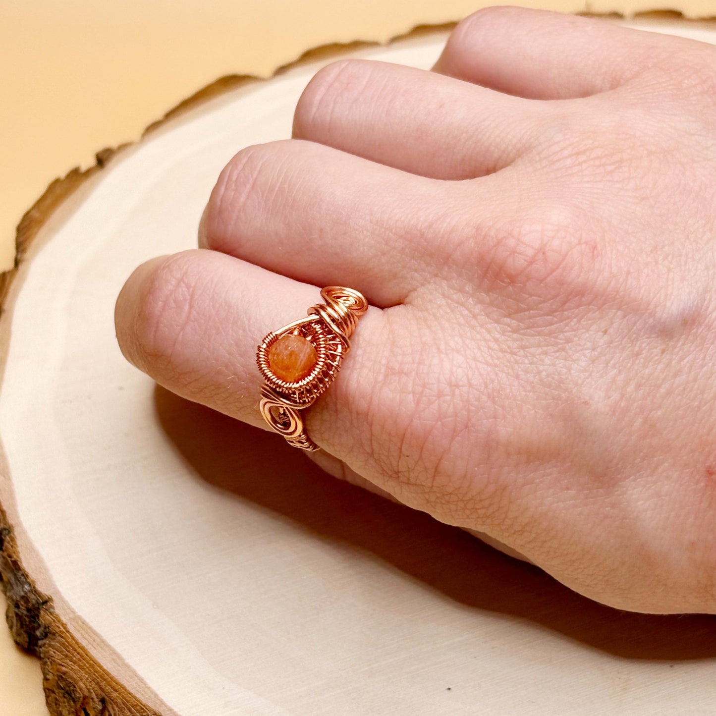 Hand wearing a copper ring with an orange stone on a wooden surface
