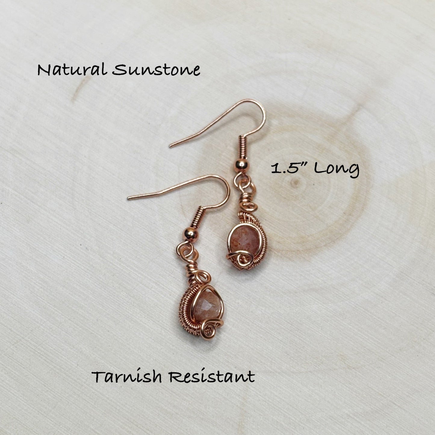 Pair of sunstone earrings with copper wire wrapping on a textured white background.