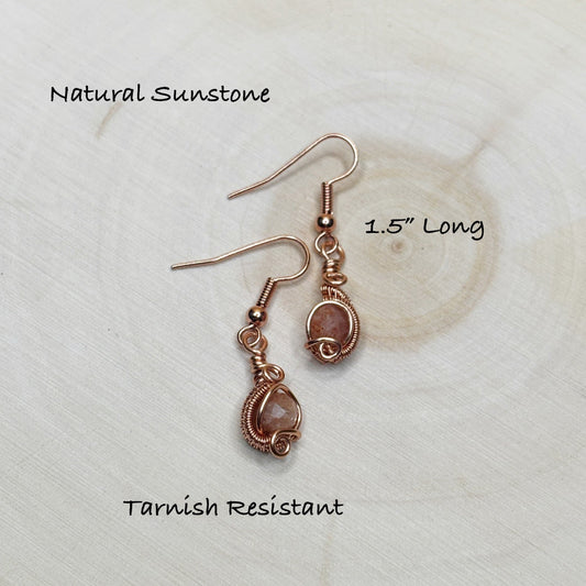 Pair of sunstone earrings with copper wire wrapping on a textured white background.