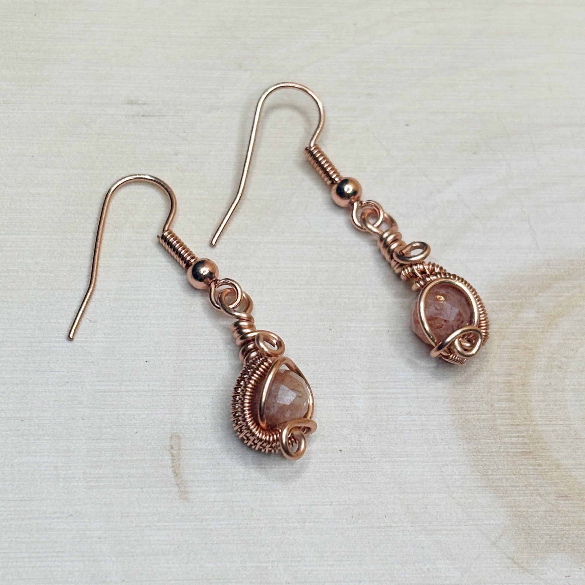 Pair of copper wire-wrapped earrings with gemstones on a light background
