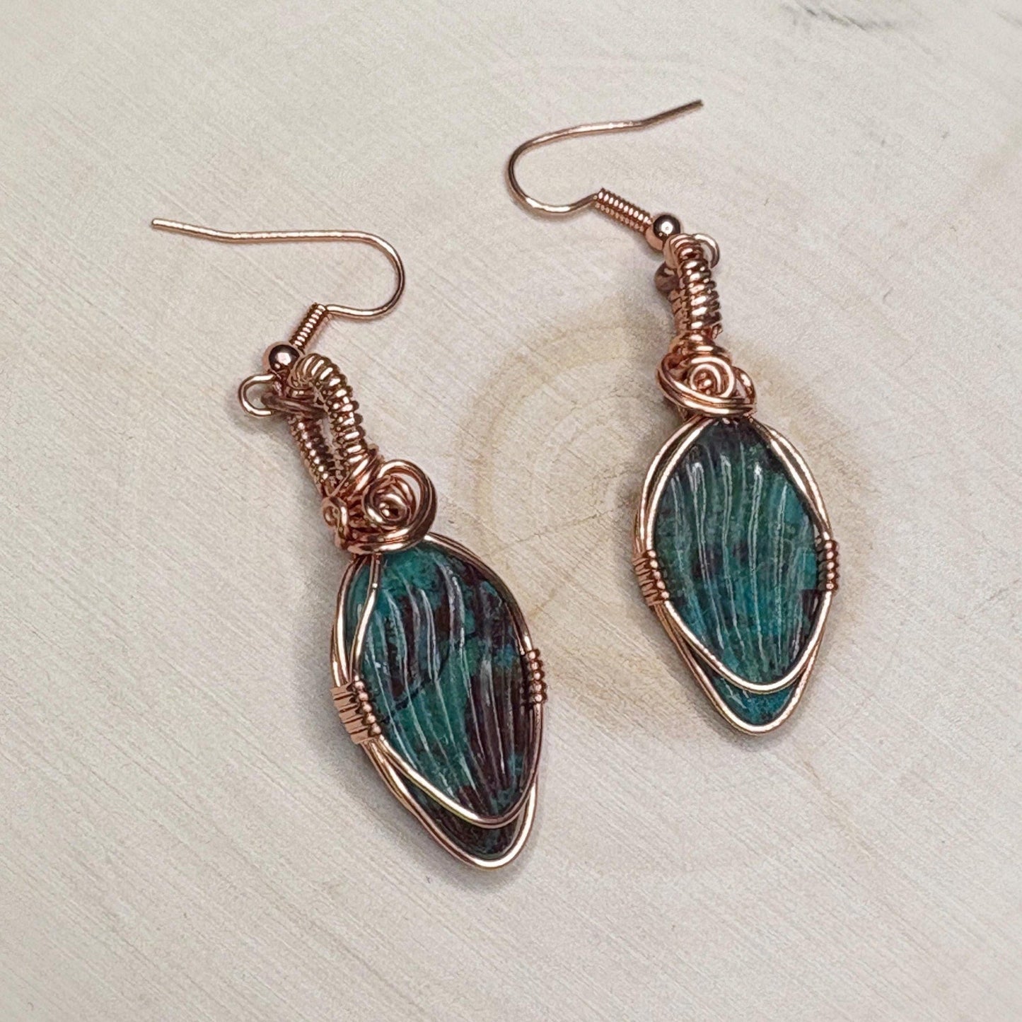 Pair of copper wire-wrapped earrings with green stone on a light background