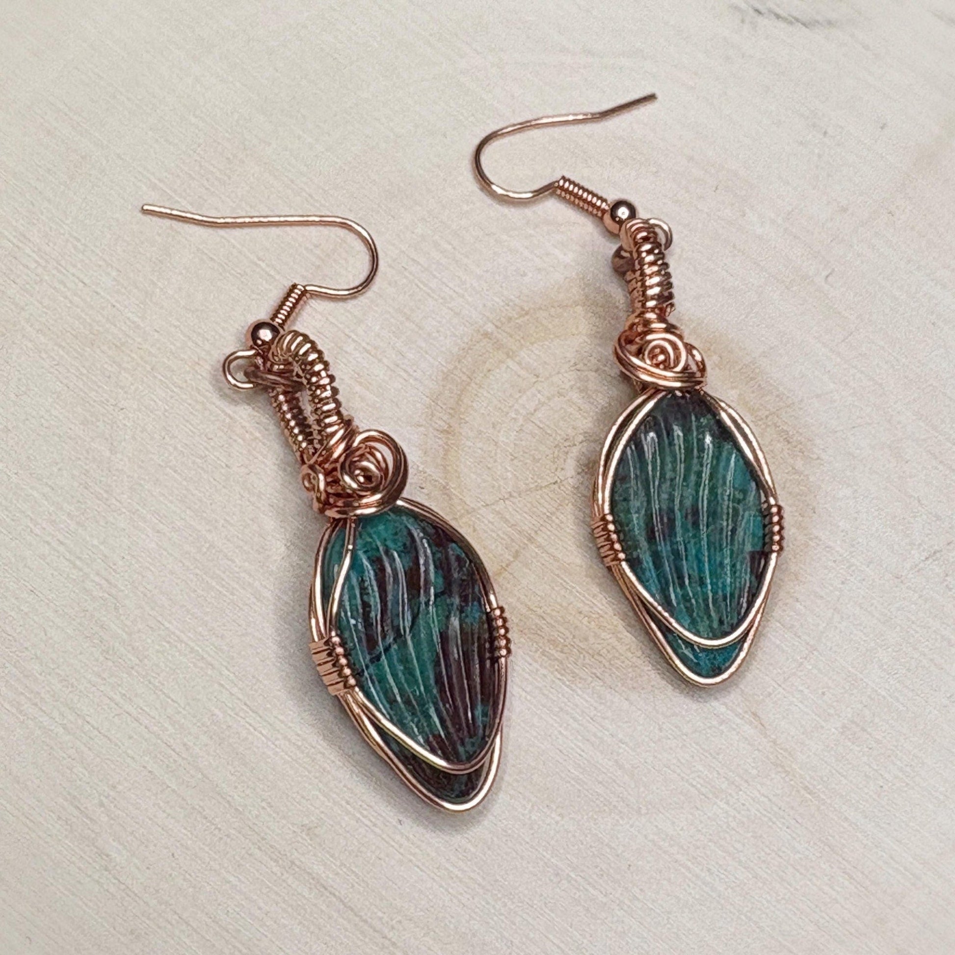Pair of copper wire-wrapped earrings with green stone on a light background