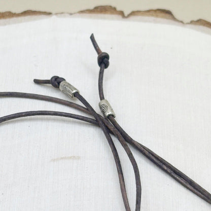 Close-up of a leather cord with metal accent beads on a textured white background