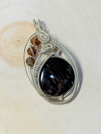 Silver wire-wrapped pendant with a dark stone and smaller stones on a light background