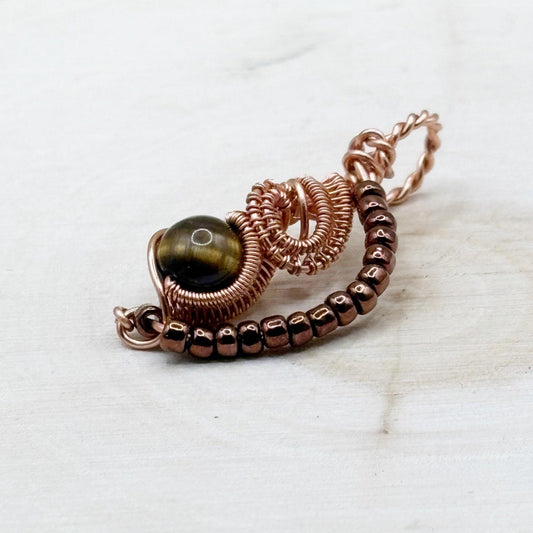 Copper wire-wrapped pendant with a sphere-shaped gemstone on a white wood background-p