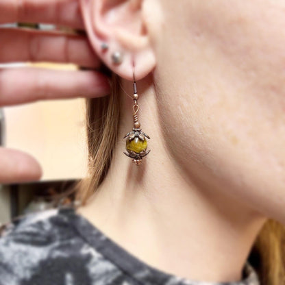 Close-up of a person wearing a detailed earring with a yellow gemstone.
