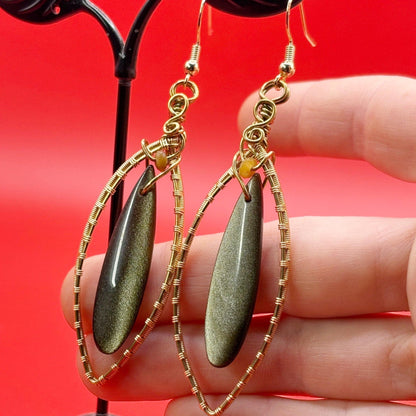 Gold wire and gold sheen teardrop earrings held against a red background