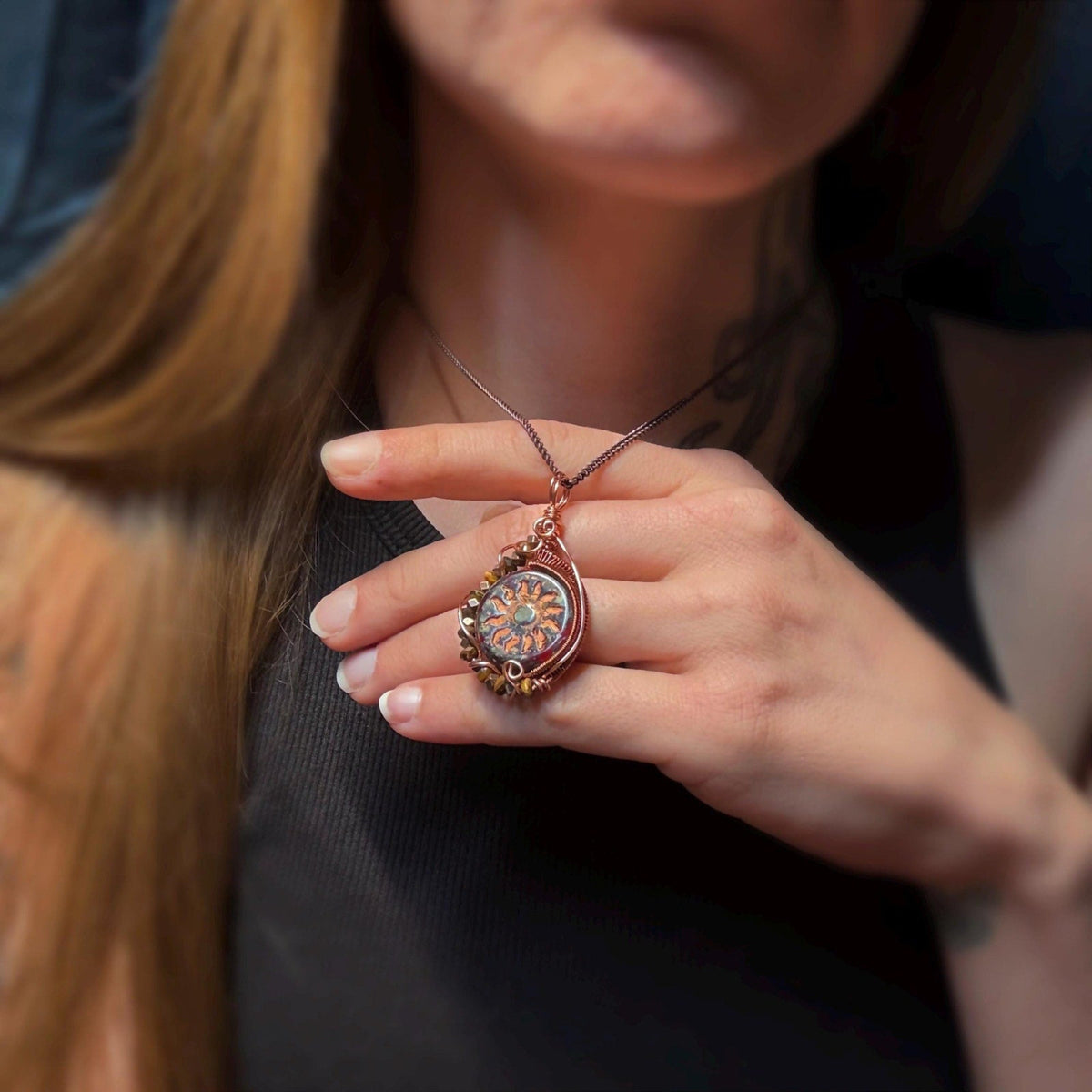 Model holding up a handmade copper wire wrap pendant to show size against hand