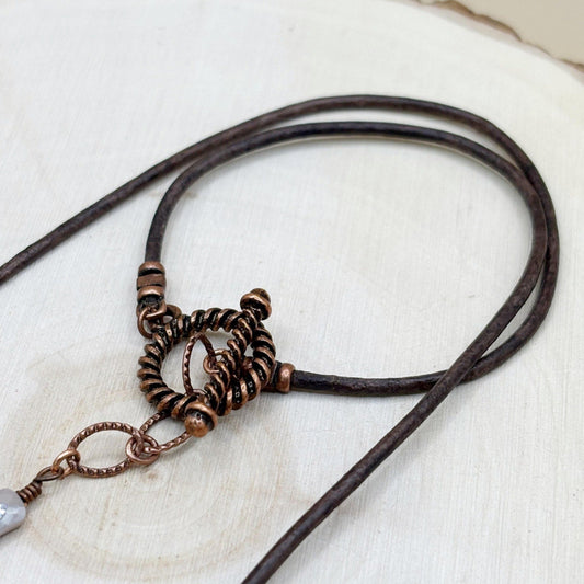 Brown leather necklace with copper metal elements on a light background