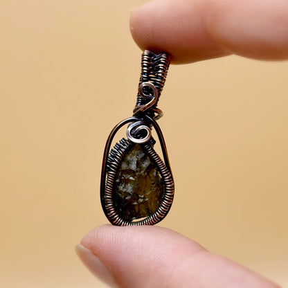 Hand holding a wire-wrapped pendant with a natural stone against a beige background