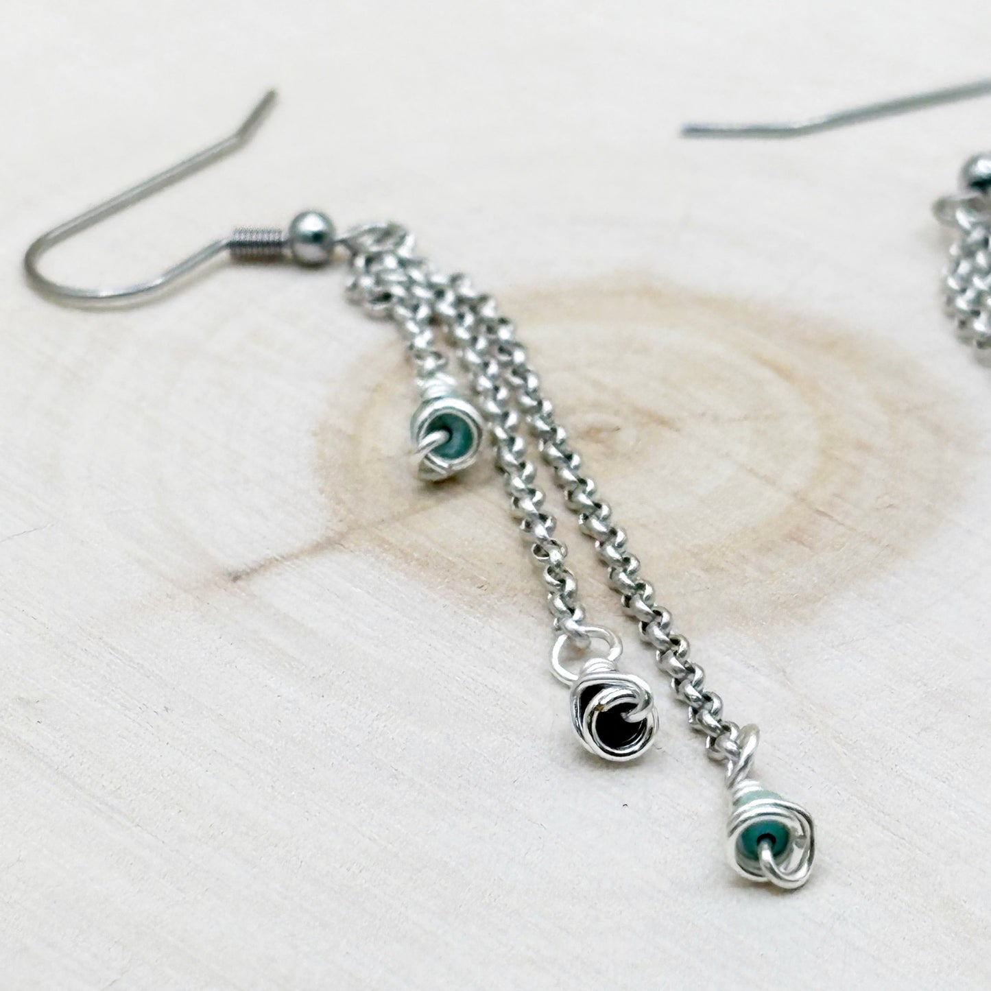 Silver chain earrings with turquoise wire wrapped charms on a light wooden surface
