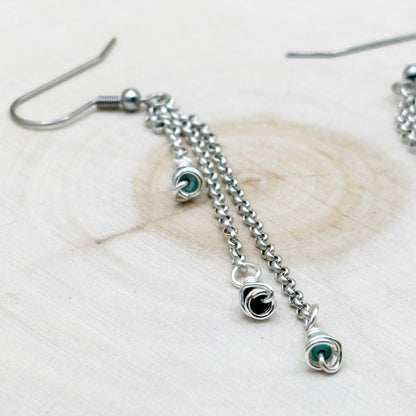 Silver chain earrings with turquoise wire wrapped charms on a light wooden surface