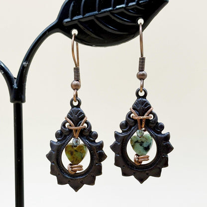 Pair of earrings with green heart-shaped stones on a black stand.