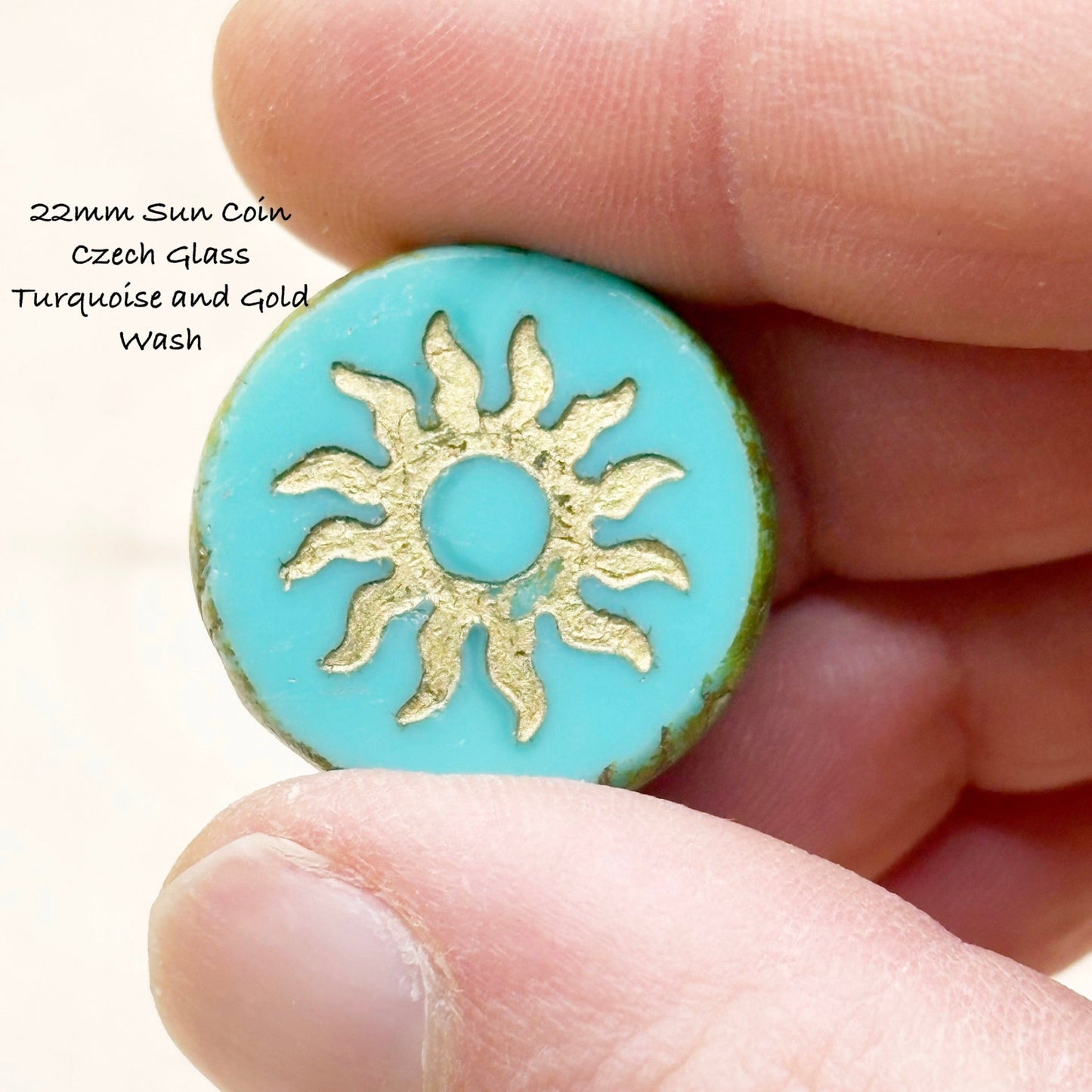 Turquoise Czech glass sun coin held between fingers with gold sun design