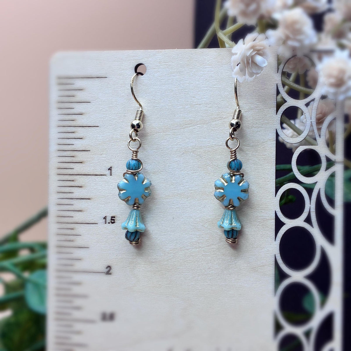 turquoise floral earrings with gold tone wire hanging on a wooden stand to show case measurement 