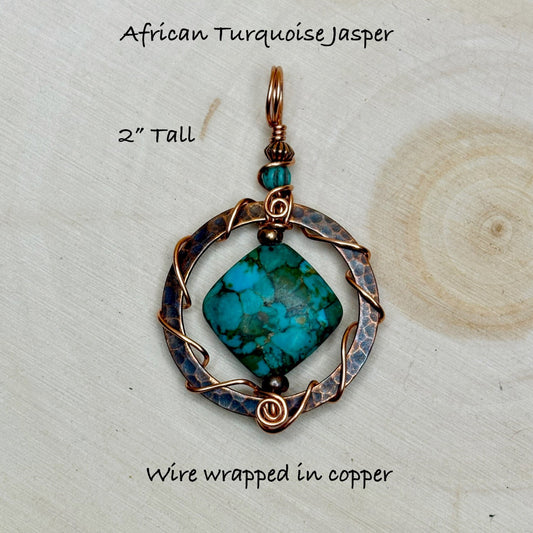 Turquoise jasper pendant with copper wire wrapping on a wooden surface
