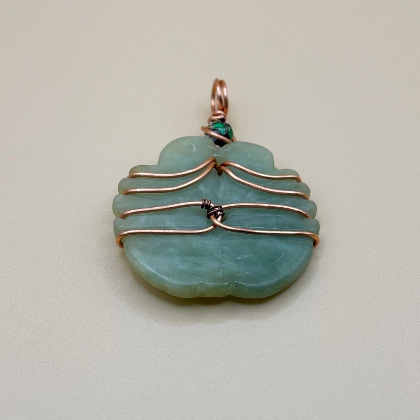 Jade pendant with copper wire wrapping on a light gray background