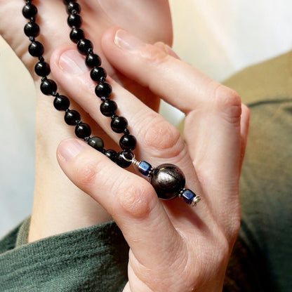 Close-up of hands holding a black beaded necklace with a blurred background