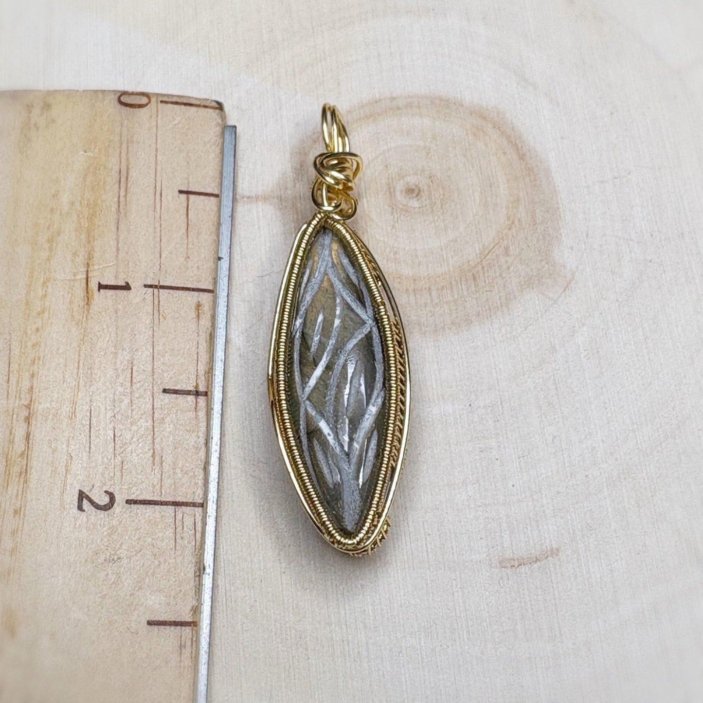Gold pendant with a stone-like center on a wooden surface with a ruler.