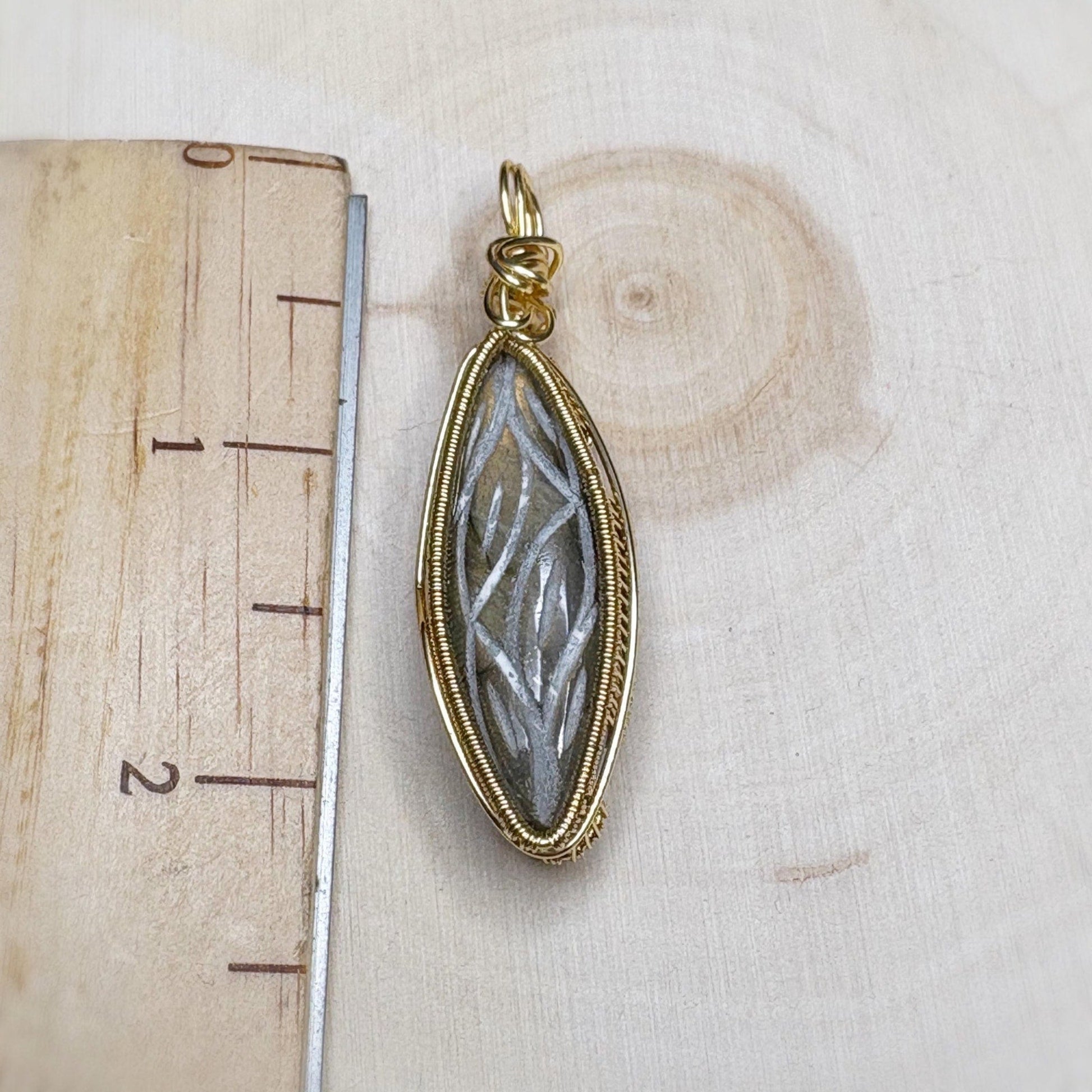 Gold pendant with a stone-like center on a wooden surface with a ruler.