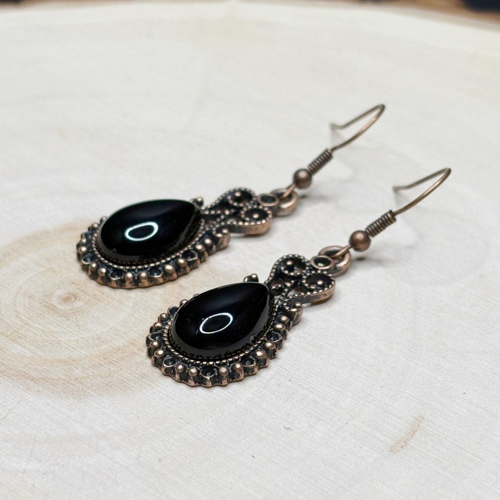 Pair of black earrings with decorative metalwork on a light wooden surface