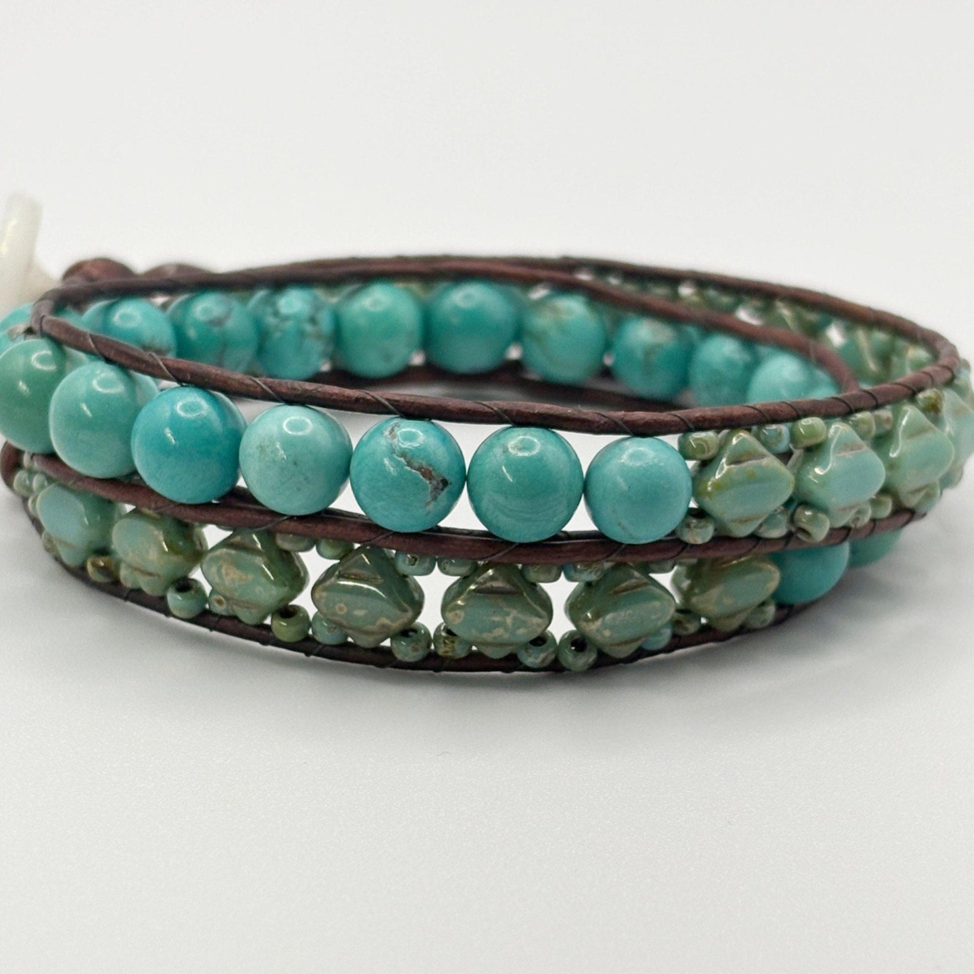 Turquoise beaded bracelet with brown leather strap on a white background