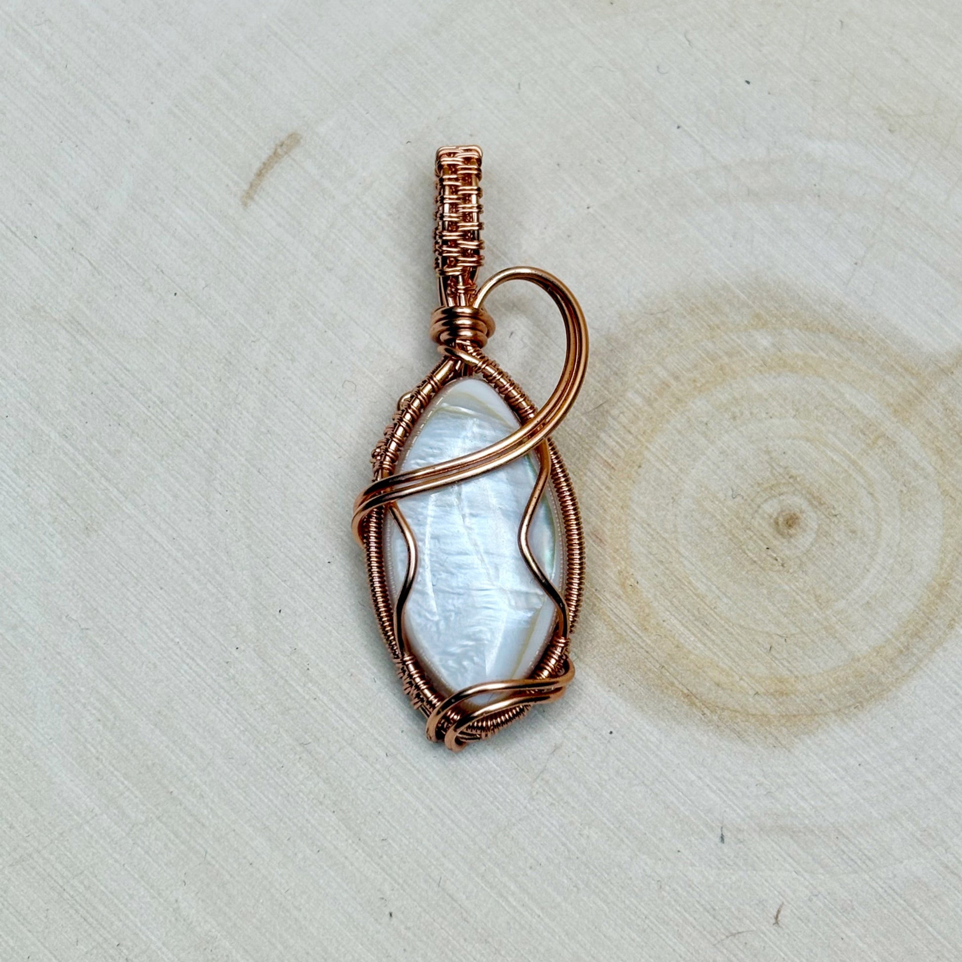 Mother of pearl shell with copper wire wrapping sitting on a light background