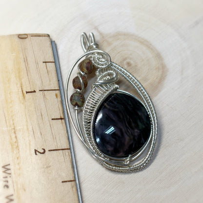 Silver wire-wrapped pendant with a dark stone on a wooden surface
