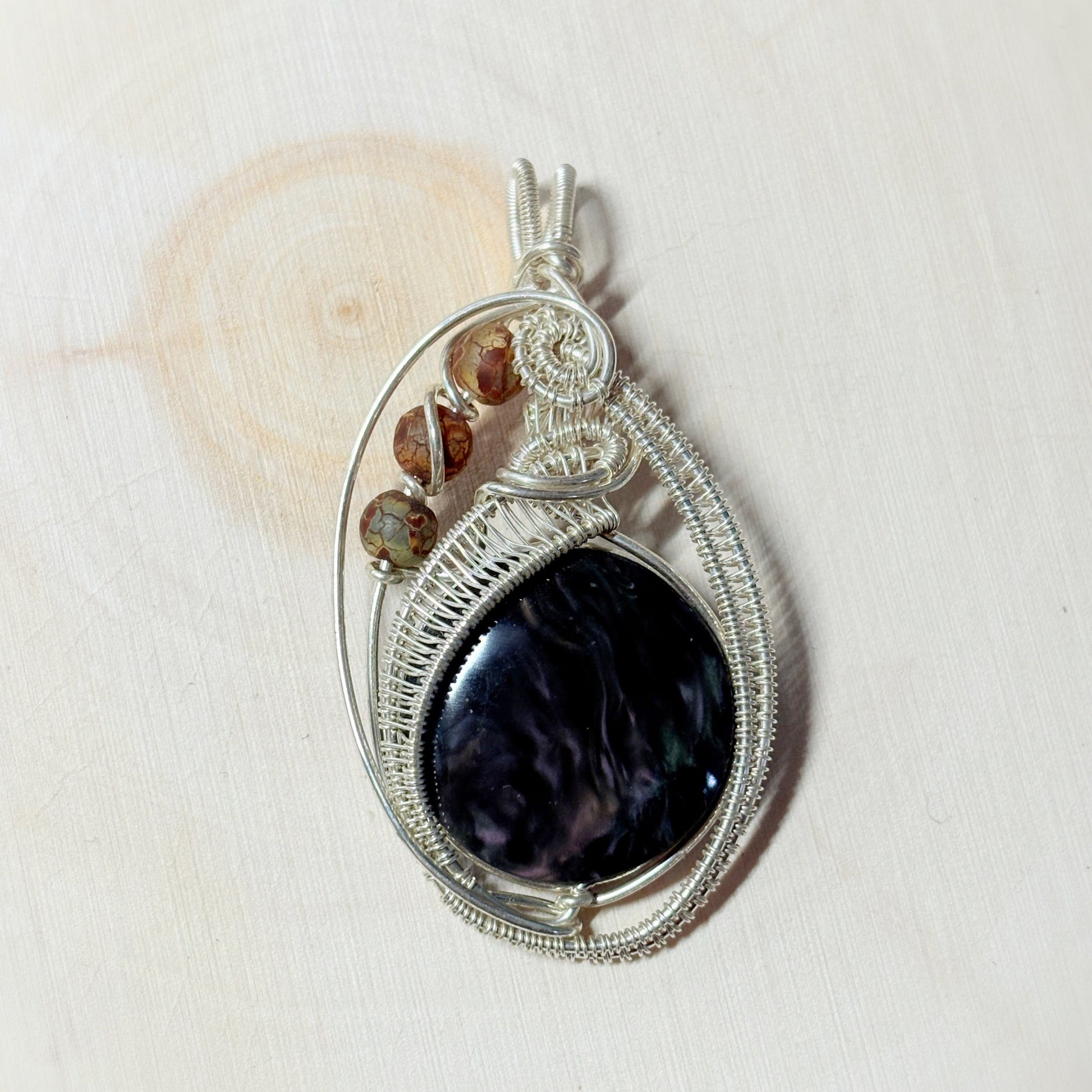 Silver wire-wrapped pendant with a dark stone and smaller brown stones on a light background
