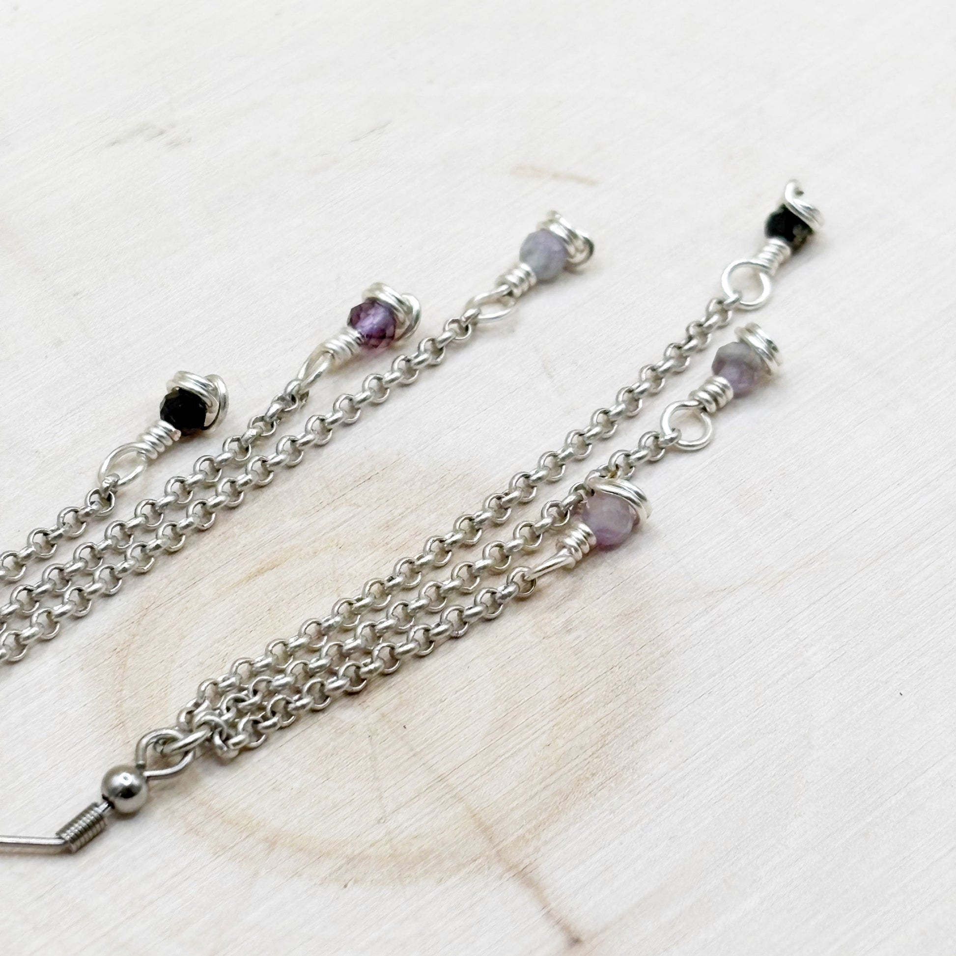 Silver chain with purple beads on a light wooden surface