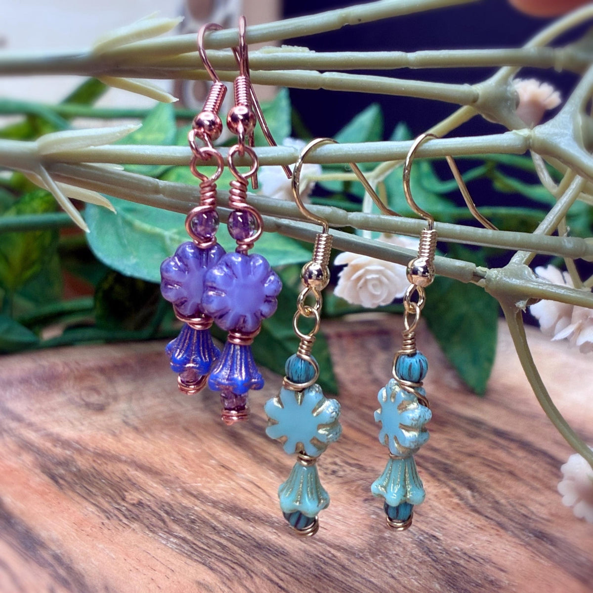 Handmade wire wrapped earrings in gold and copper with floral beads hanging on a branch