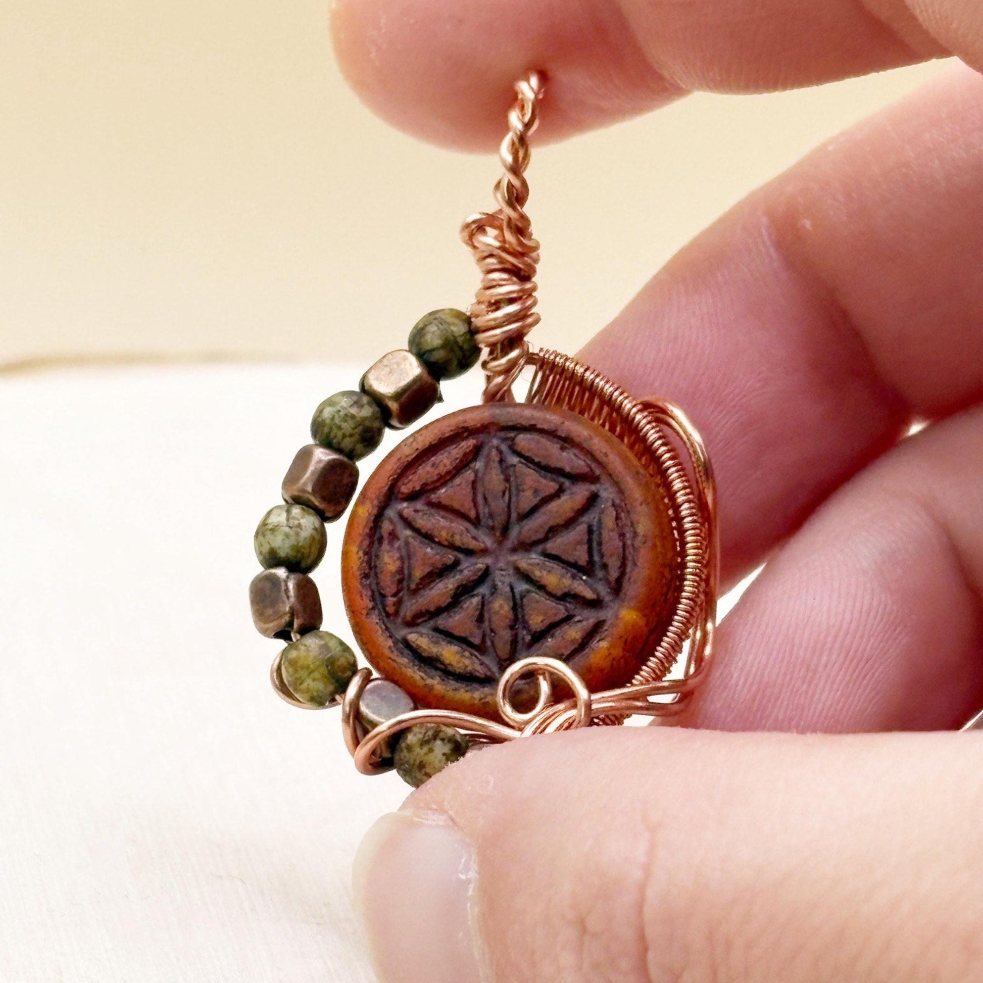 Red Tone Glass bead with copper wire wrapping being held against a neutral background