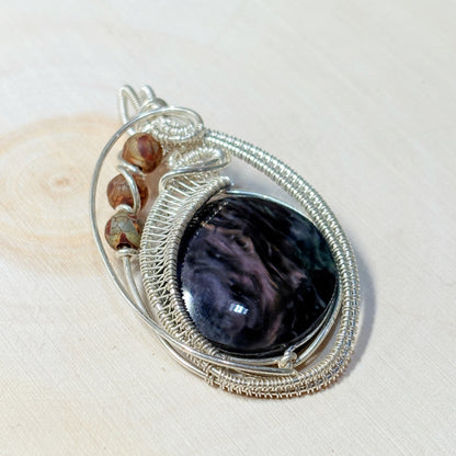 Silver wire-wrapped pendant with a dark stone and smaller stones on a light background