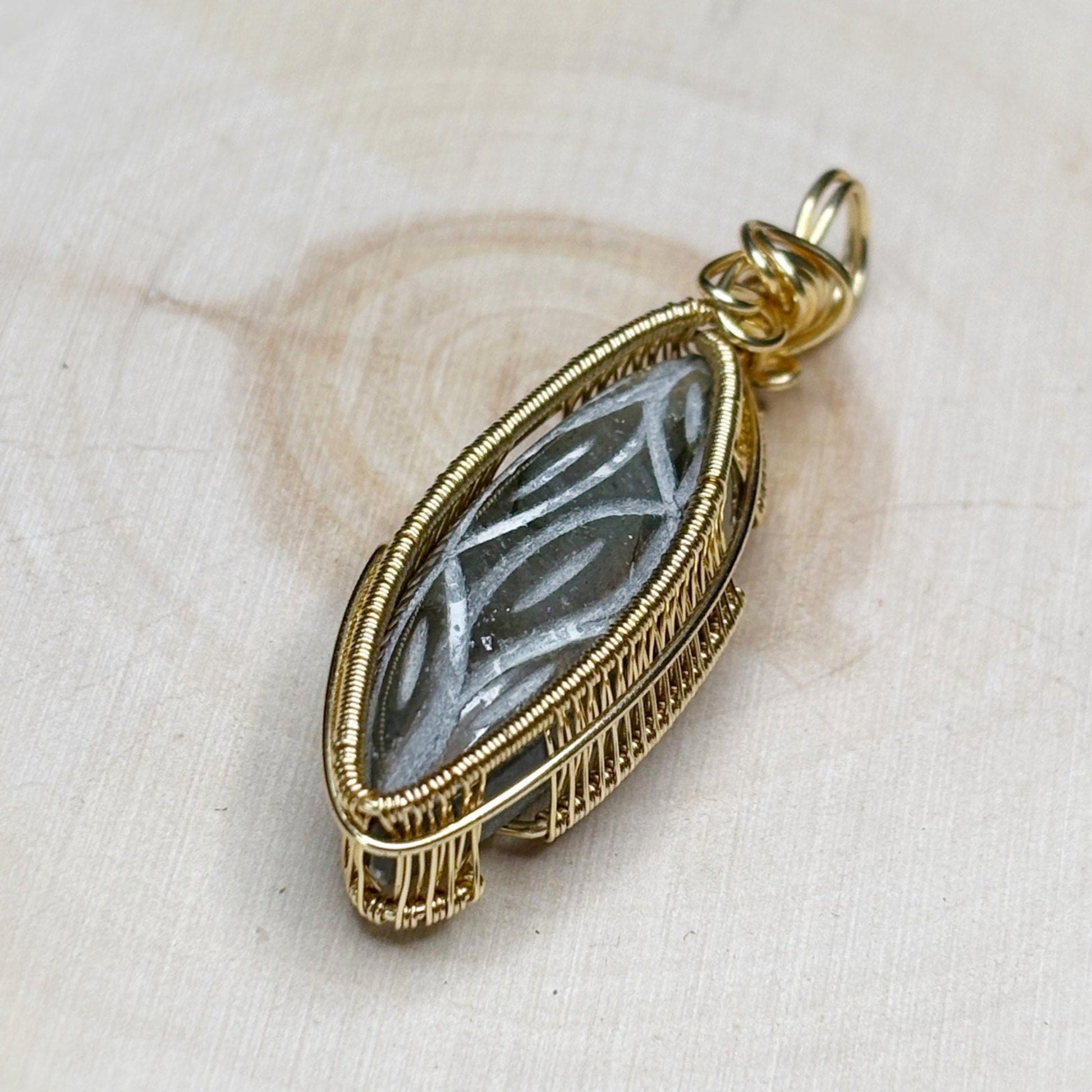 Gold-framed pendant with a central stone on a beige fabric background
