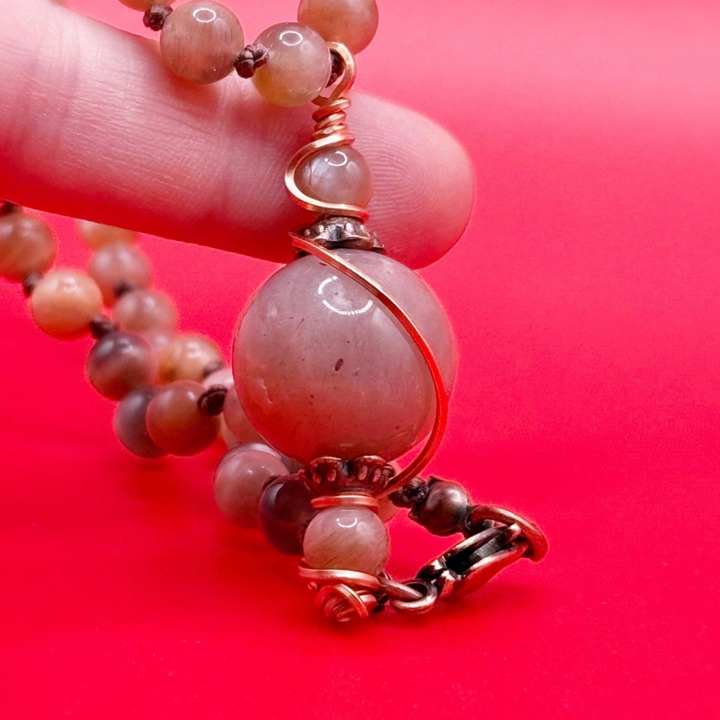 Close-up of a beaded necklace with a large pink bead on a red background