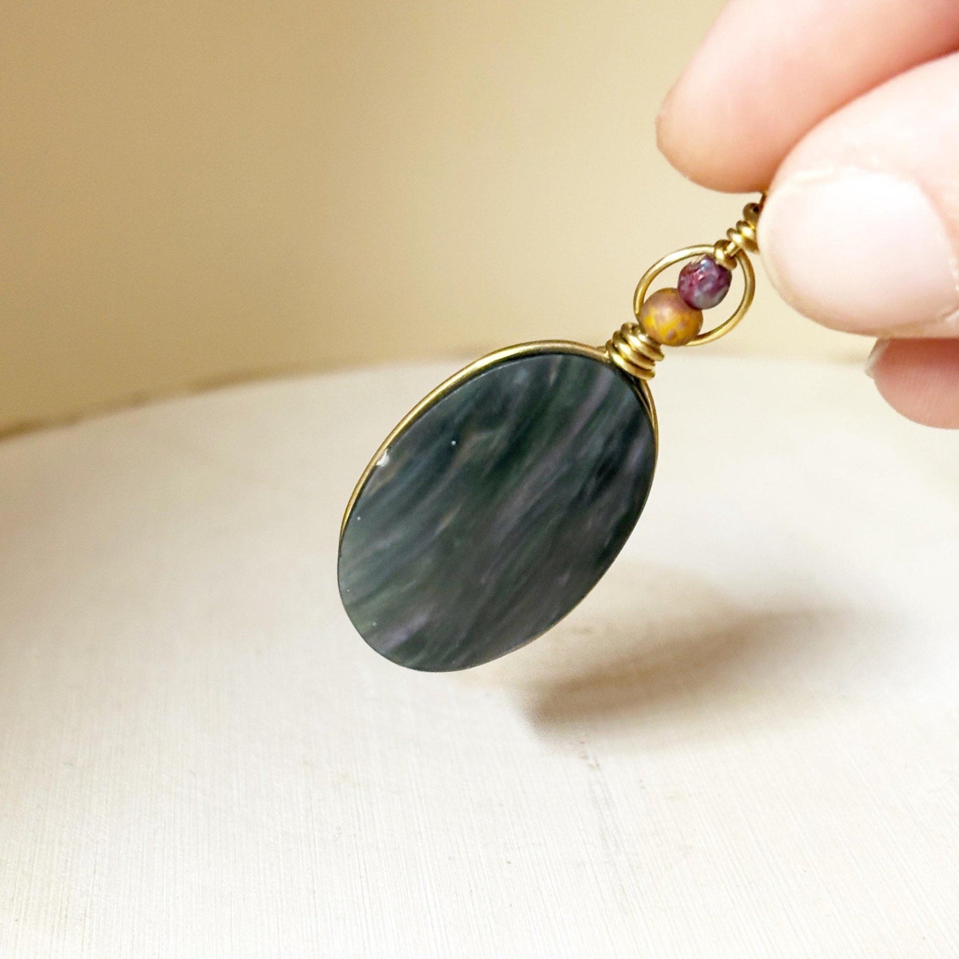 Hand holding a pendant with a dark green stone and gold accents.