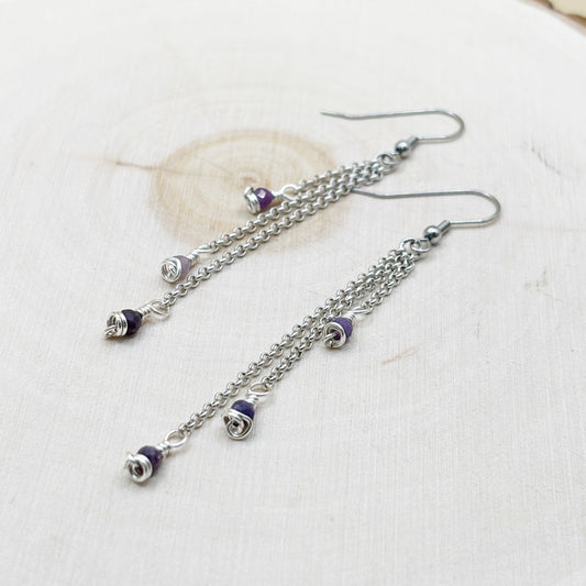 Silver chain earrings with purple beads on a wood background-p
