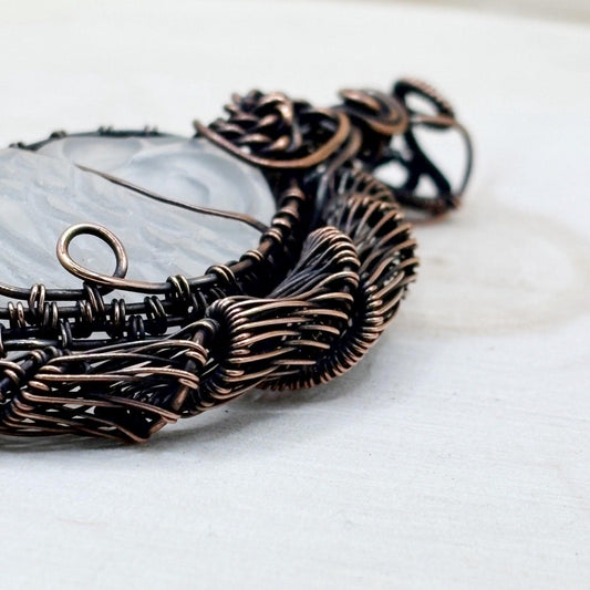 copper wire-wrapped necklace pendant with a clear quartz crystal carved owl on a white wood background