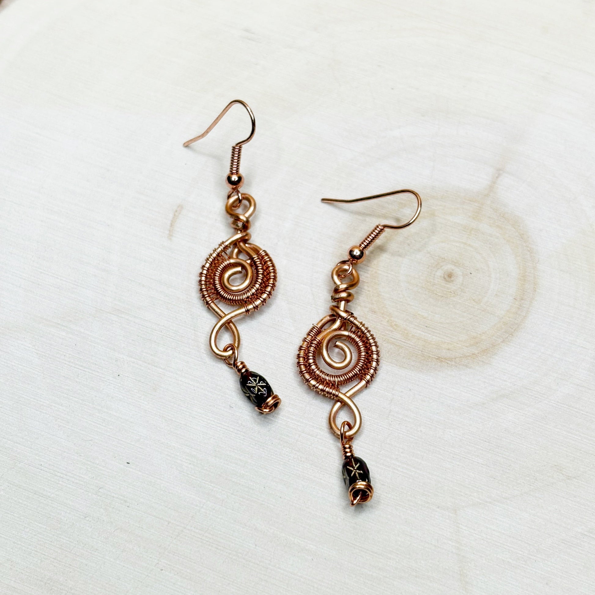 Copper wire-wrapped earrings with black beads on a white background