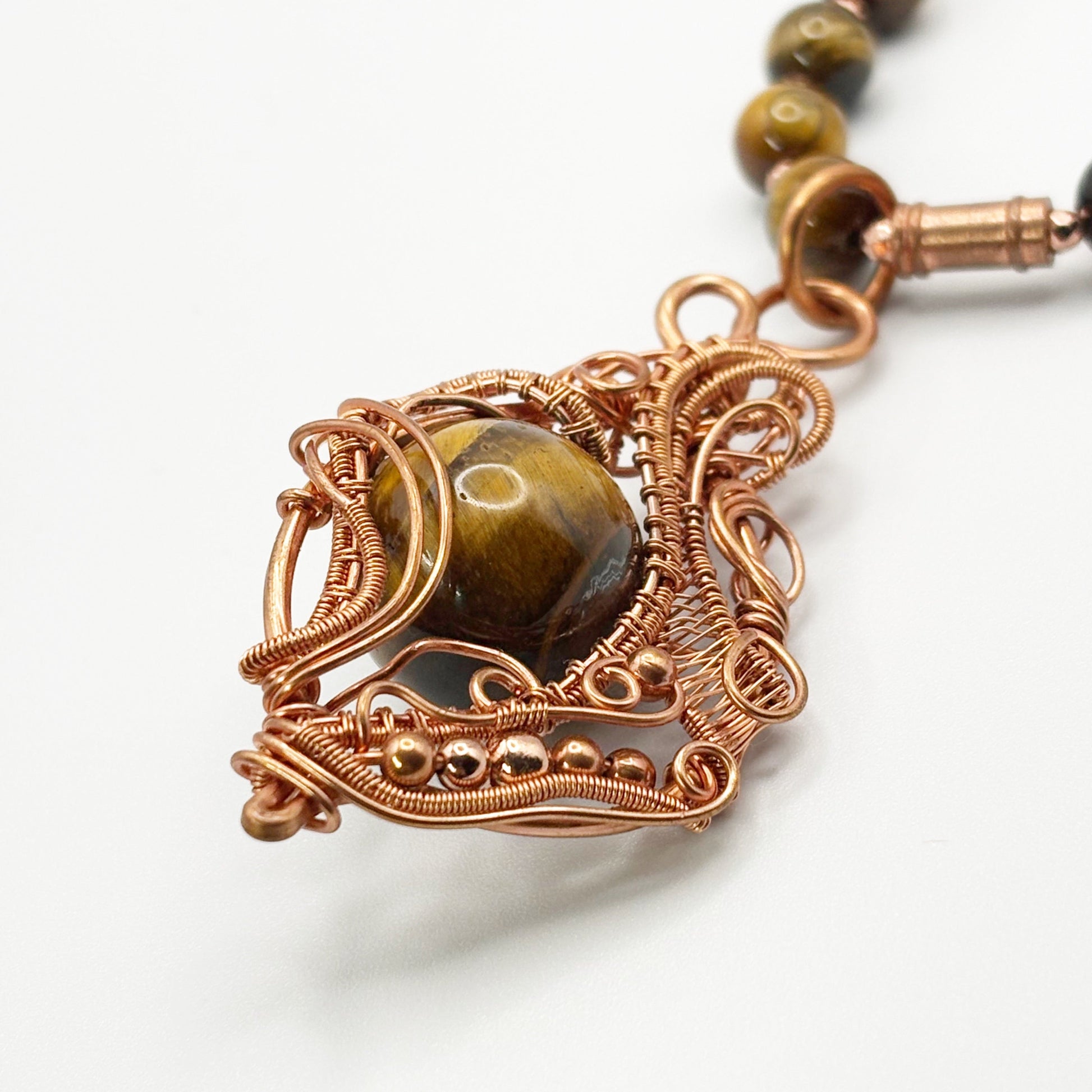 Jewelry with a copper wire-wrapped pendant featuring a central stone on a white background