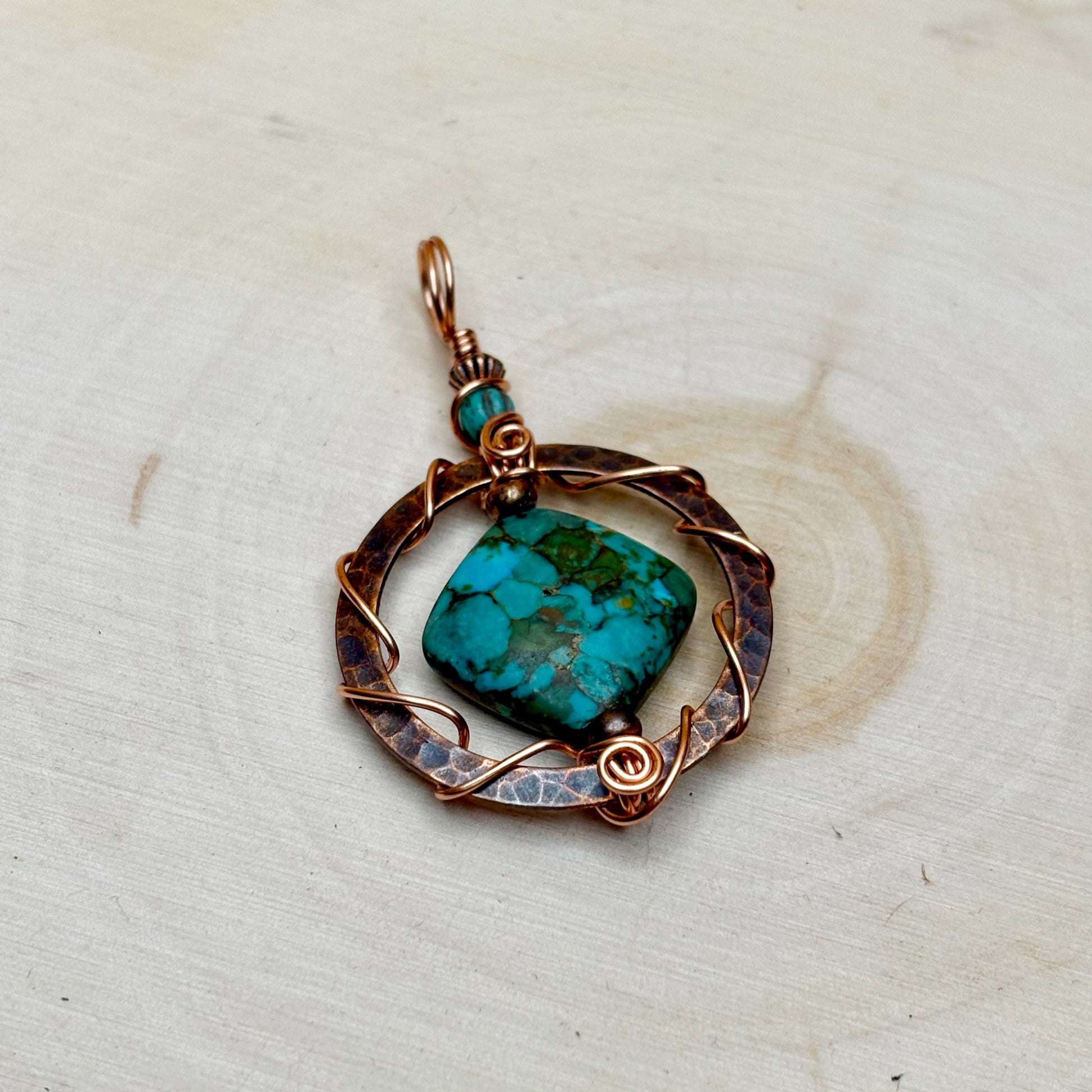 Turquoise stone pendant with copper wirework on a light wooden background