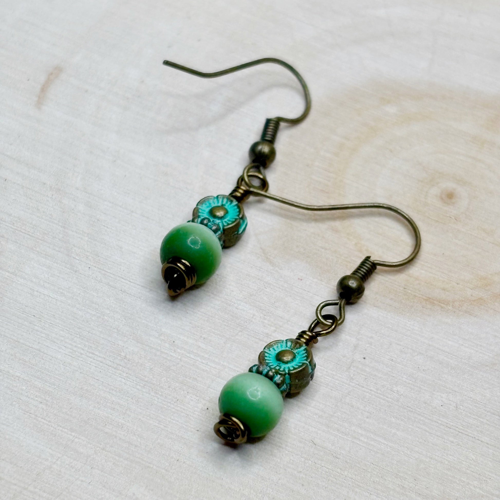 Pair of earrings with green beads and bronze hooks on a light wooden surface