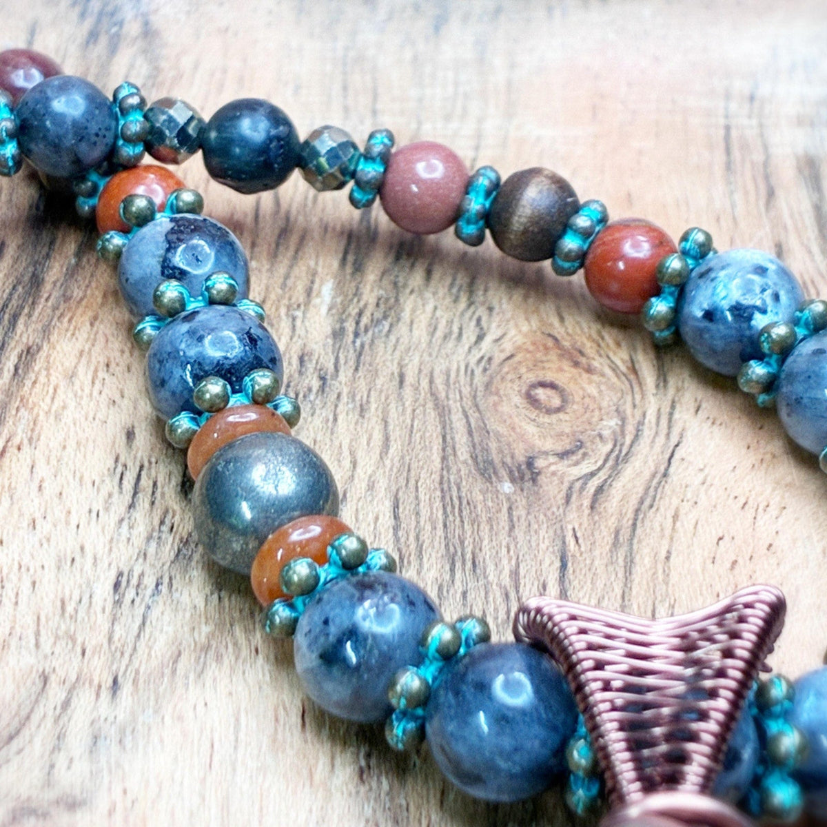 Beaded necklace on a wooden background showing reds, browns, gold, and bronze embellishments