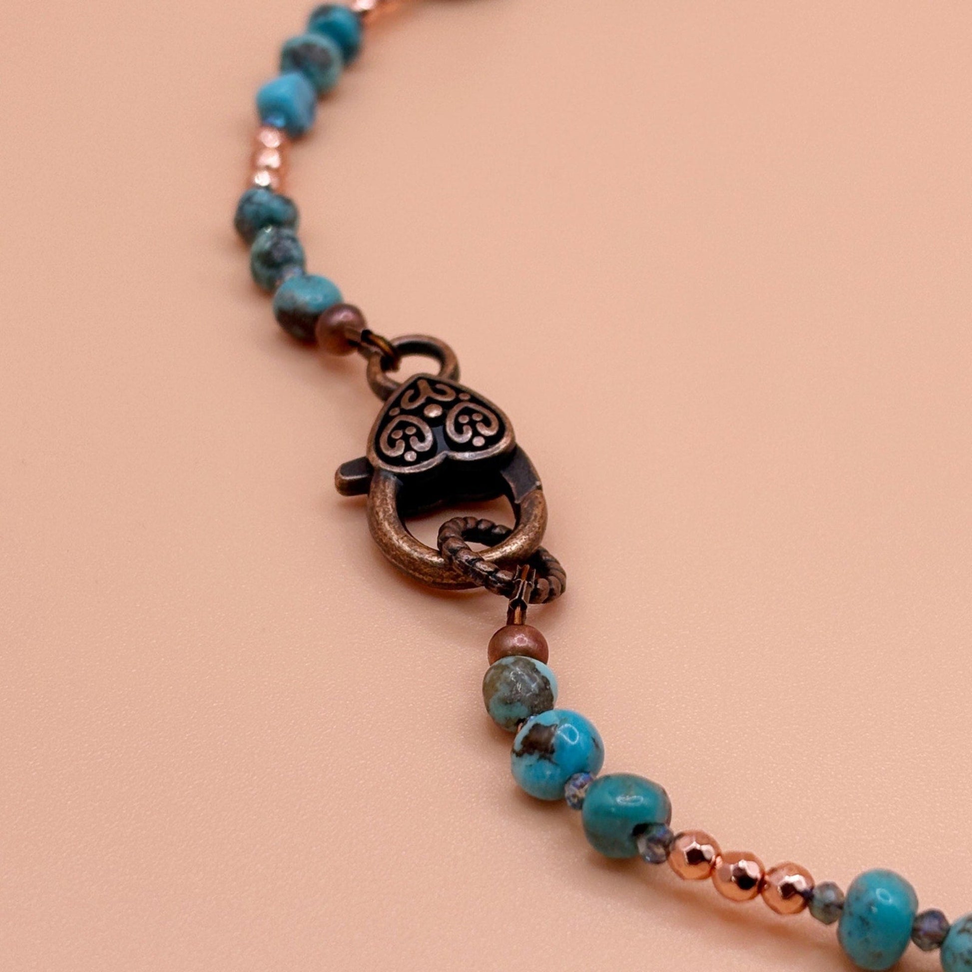 Necklace with turquoise beads and bronze clasp on a beige background