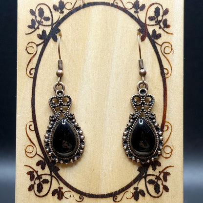 Pair of black teardrop earrings with silver detailing on a decorative wooden card.
