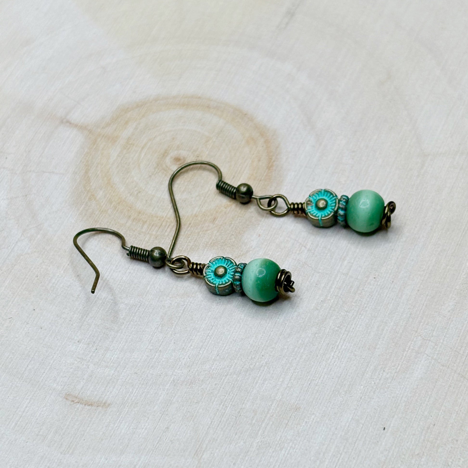 Pair of earrings with green patina beads on a textured white background