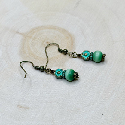Pair of earrings with green patina beads on a textured white background