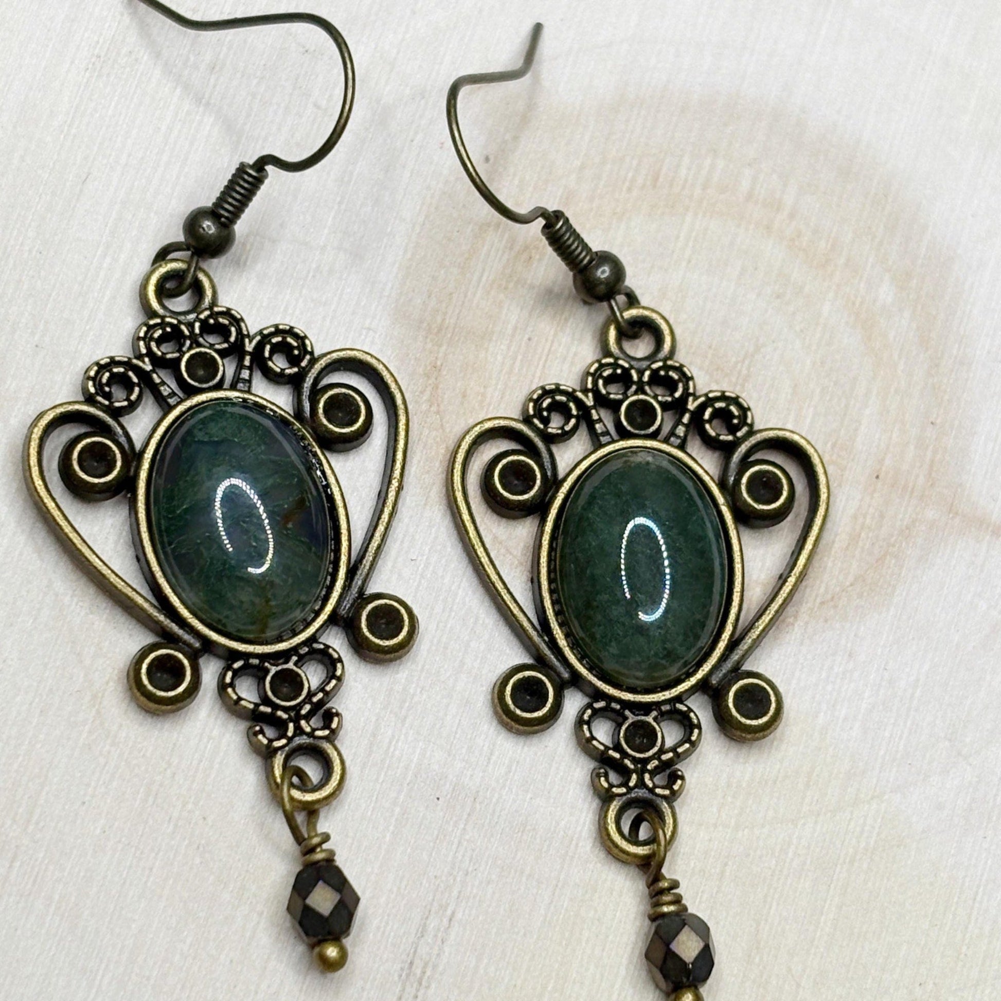 Pair of ornate earrings with green stones on a white wood background