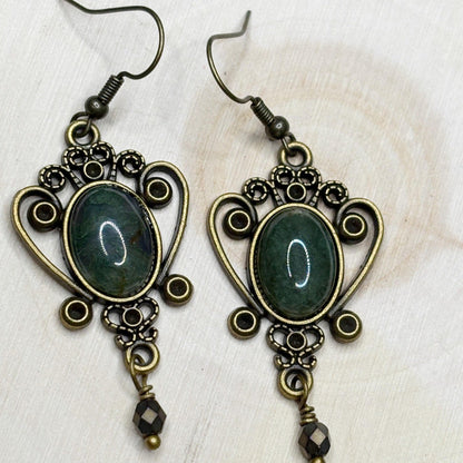 Pair of ornate earrings with green stones on a white wood background