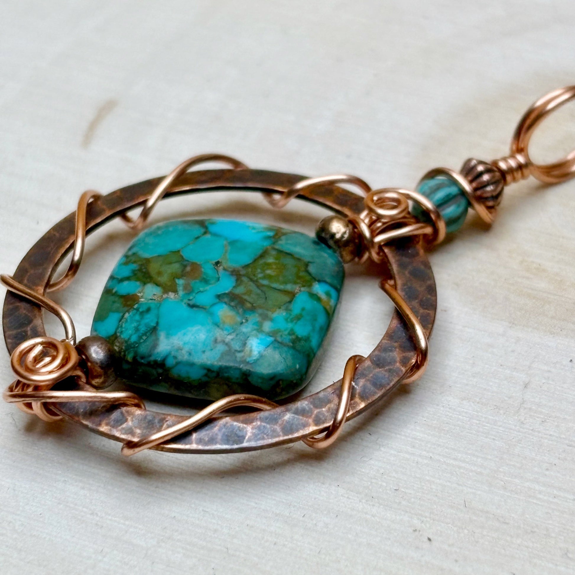Turquoise stone pendant with copper wirework on a light background